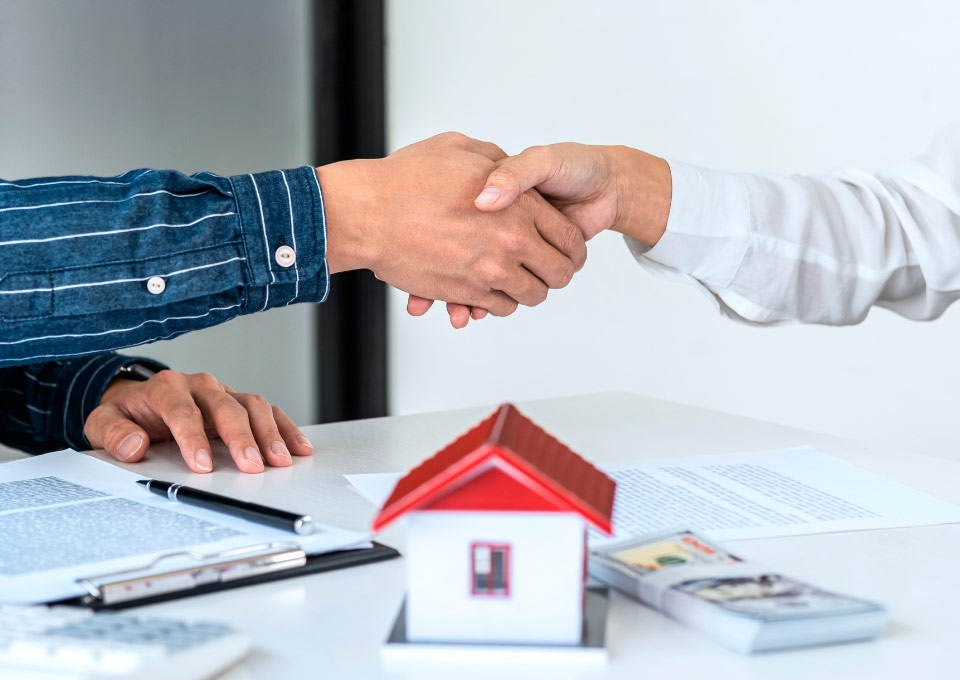 Copropiedad Inmobiliaria Dos manos estrechándose encima de documentos y un modelo de una casa